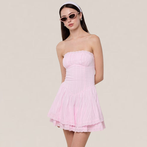 Woman wearing a light pink strapless dress against a plain background