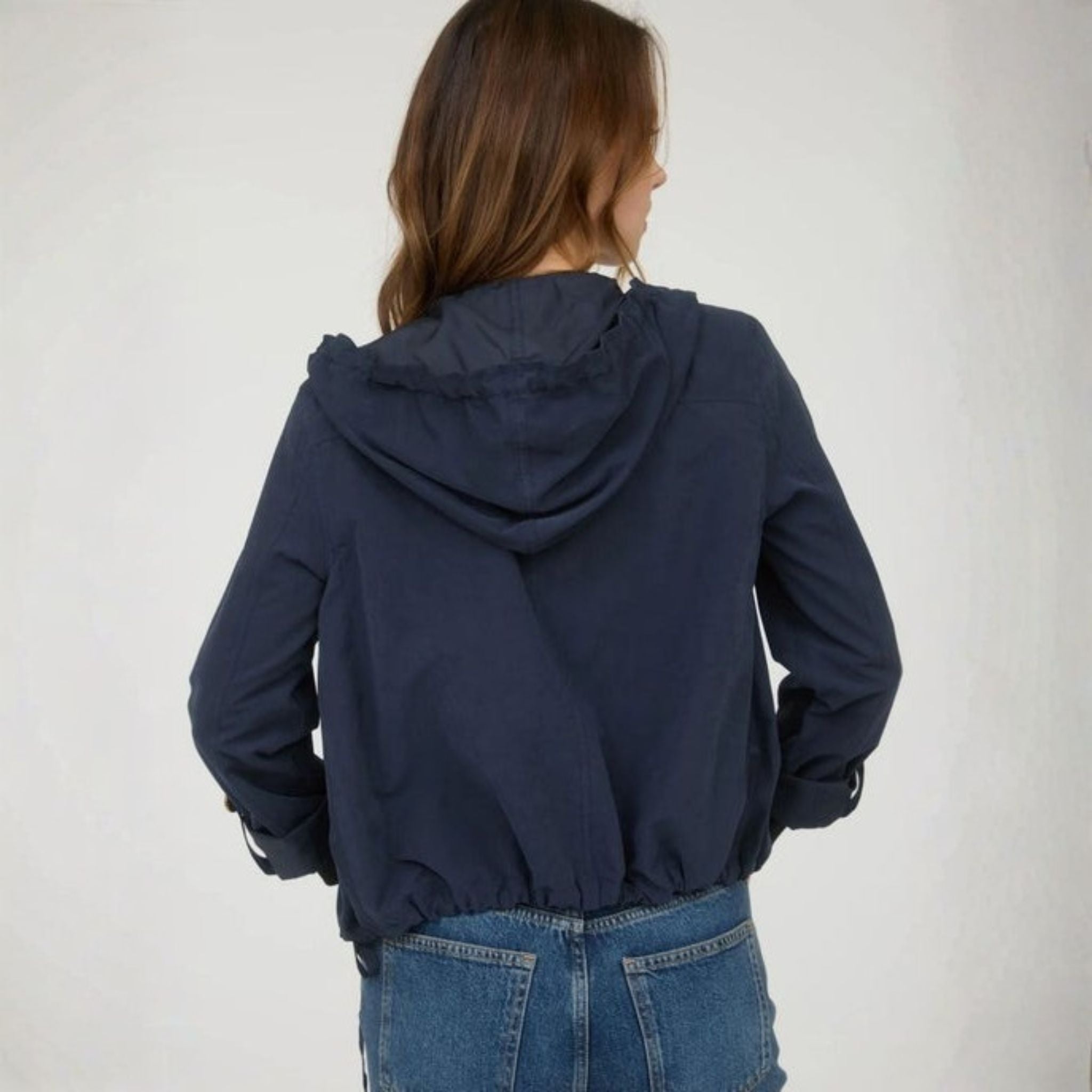 Person wearing a navy blue hooded jacket and jeans on a plain background