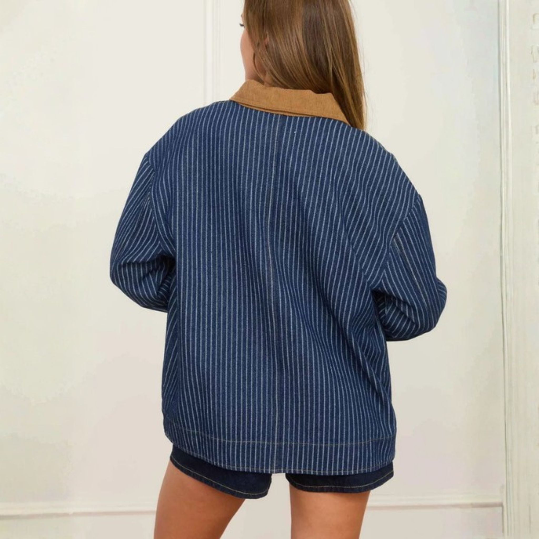 Person wearing a blue pinstripe jacket with a beige collar against a white background