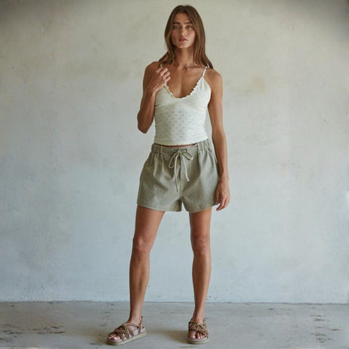 Woman wearing a white tank top and green shorts against a plain background
