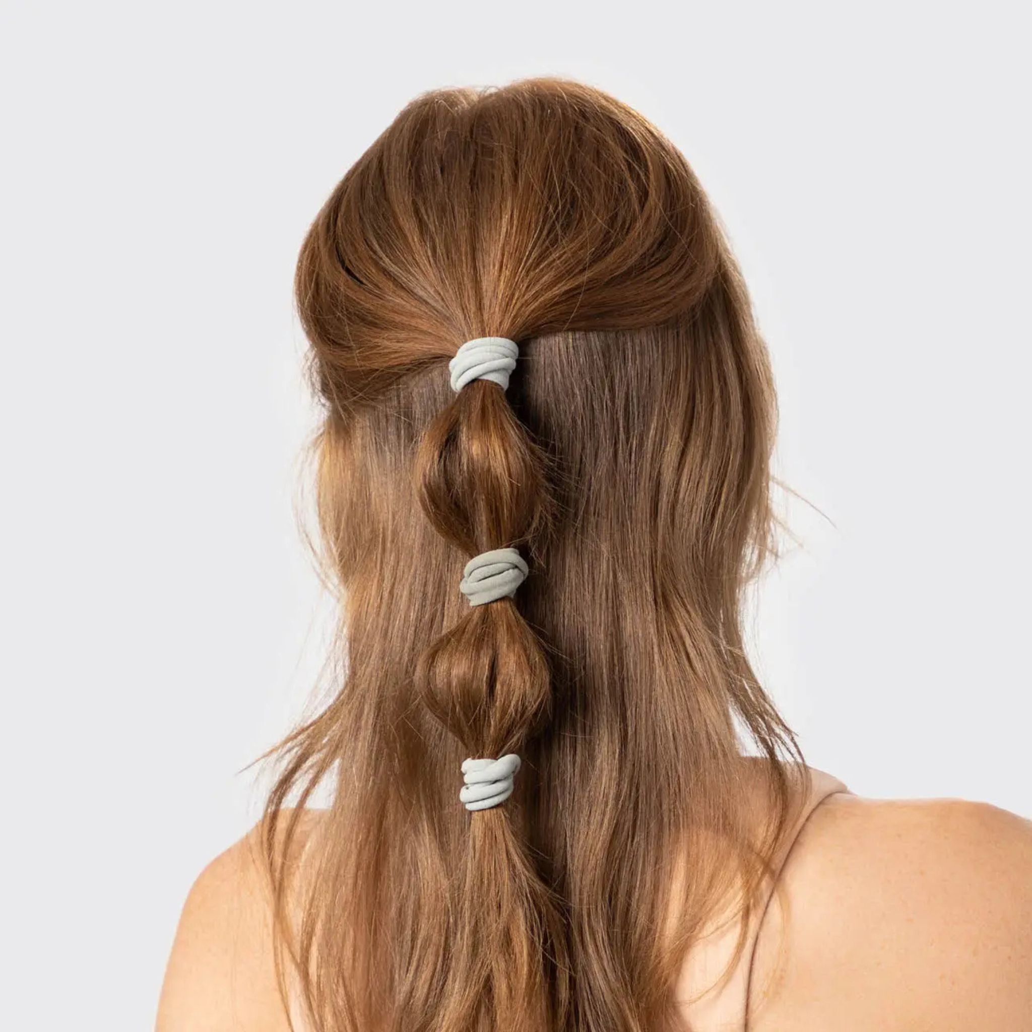 Long brown hair styled in a ponytail with white hair ties on a light gray background