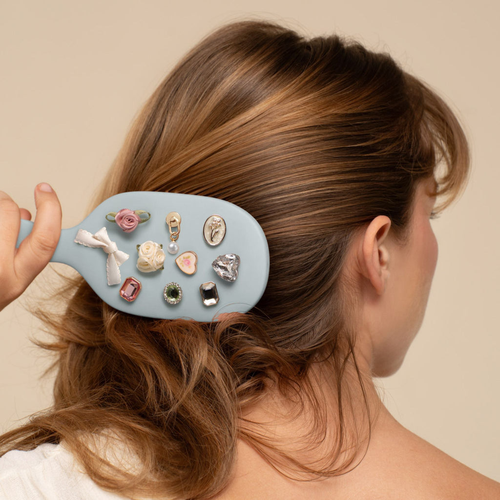 Person using a hairbrush with decorative clips on a plain background