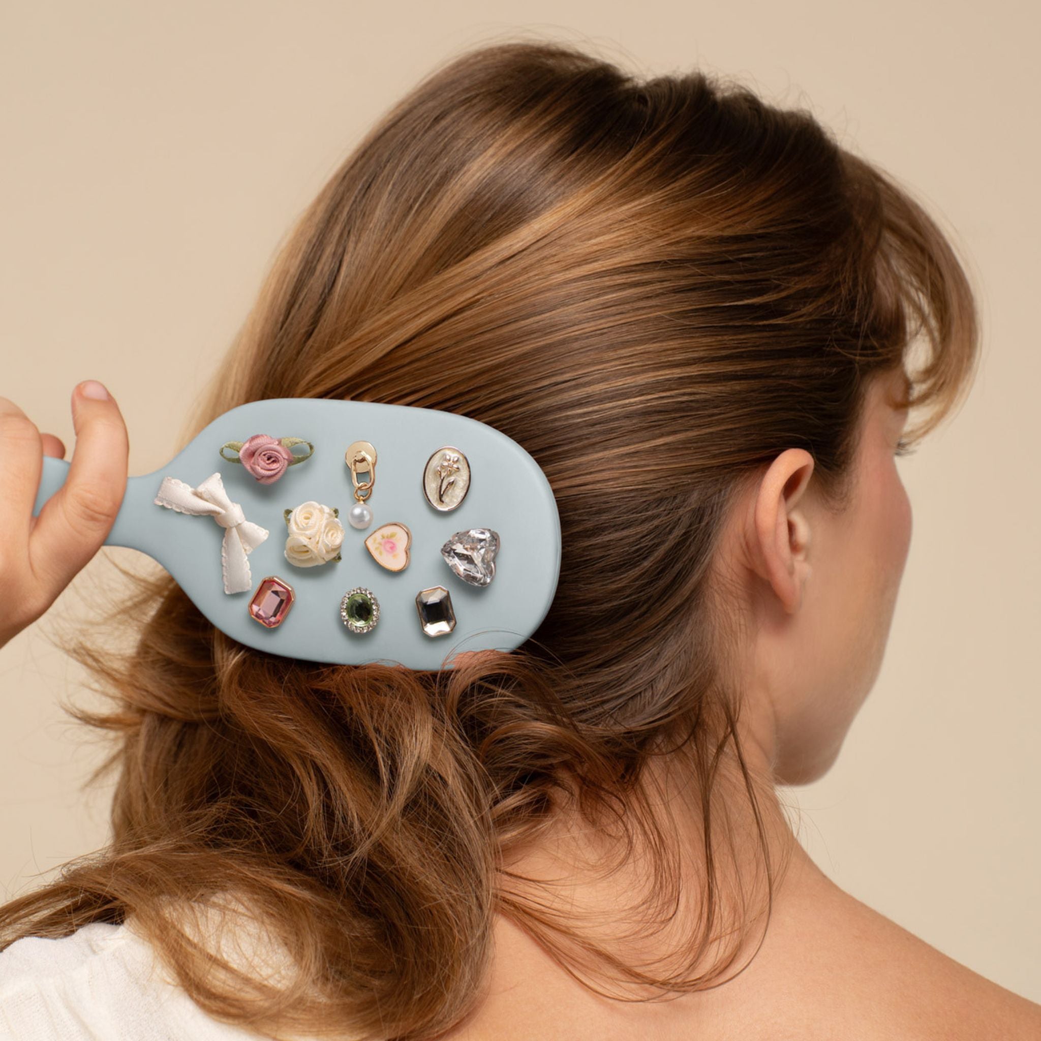 Person using a hairbrush with decorative clips on a plain background