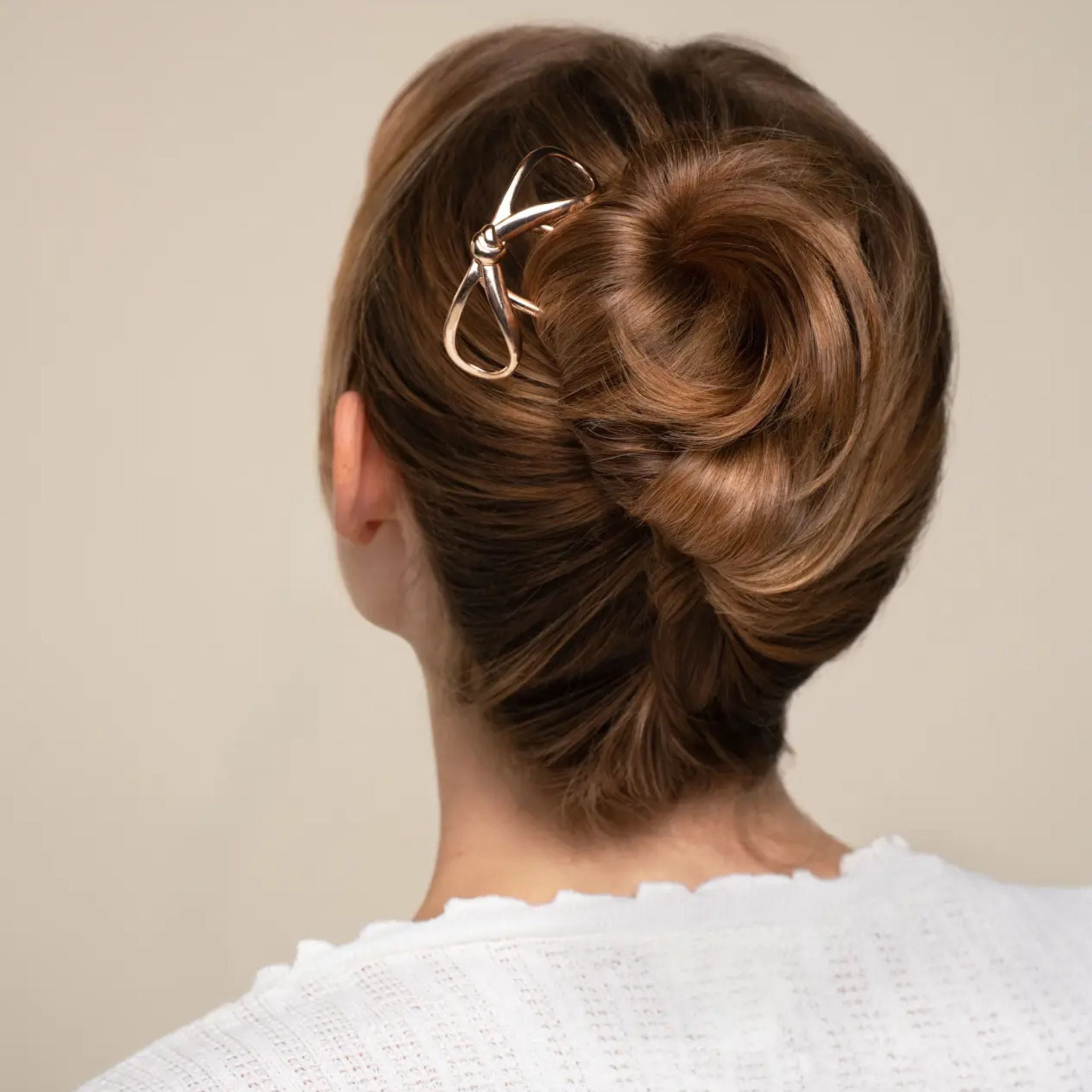Woman with styled hair bun and decorative hair clip on neutral background