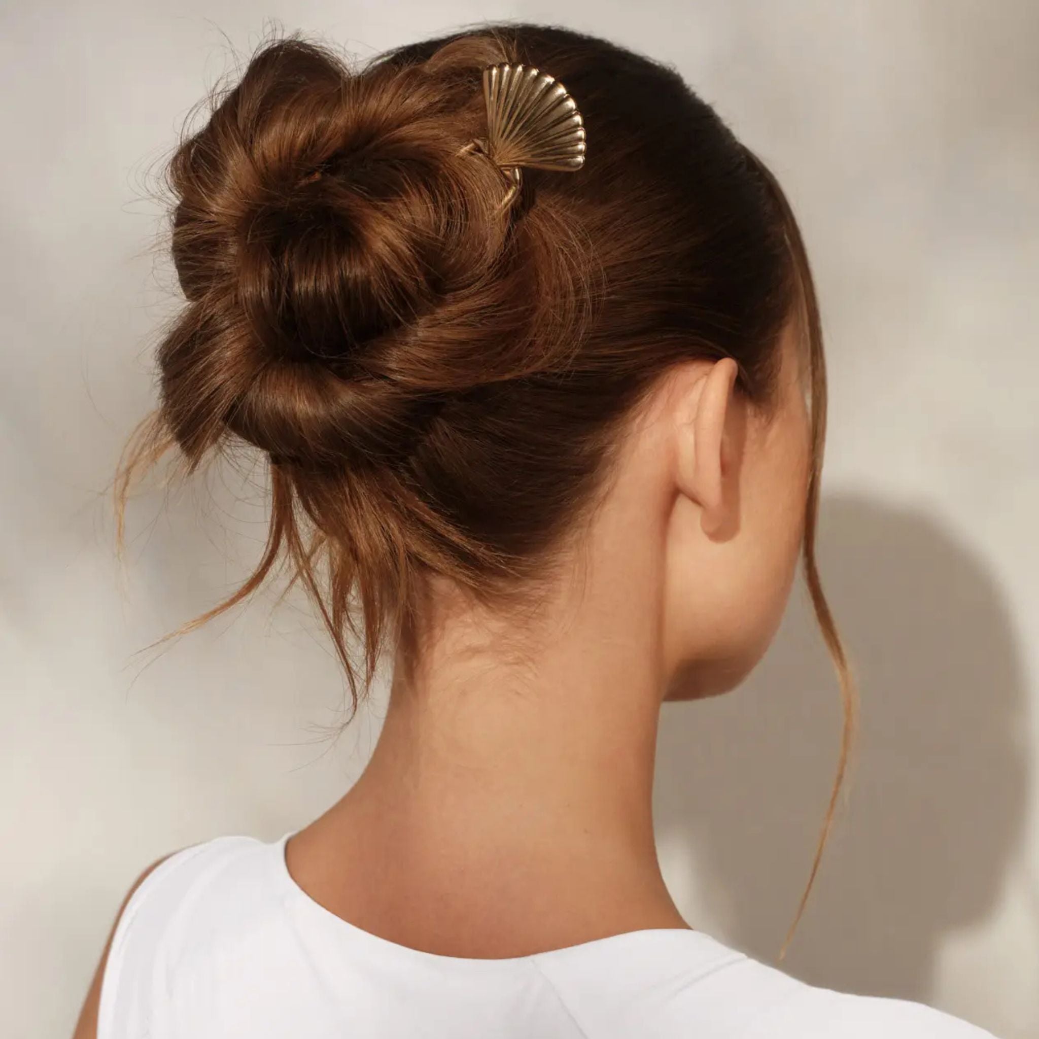Woman with a stylish hair bun adorned with a decorative hair clip against a neutral background