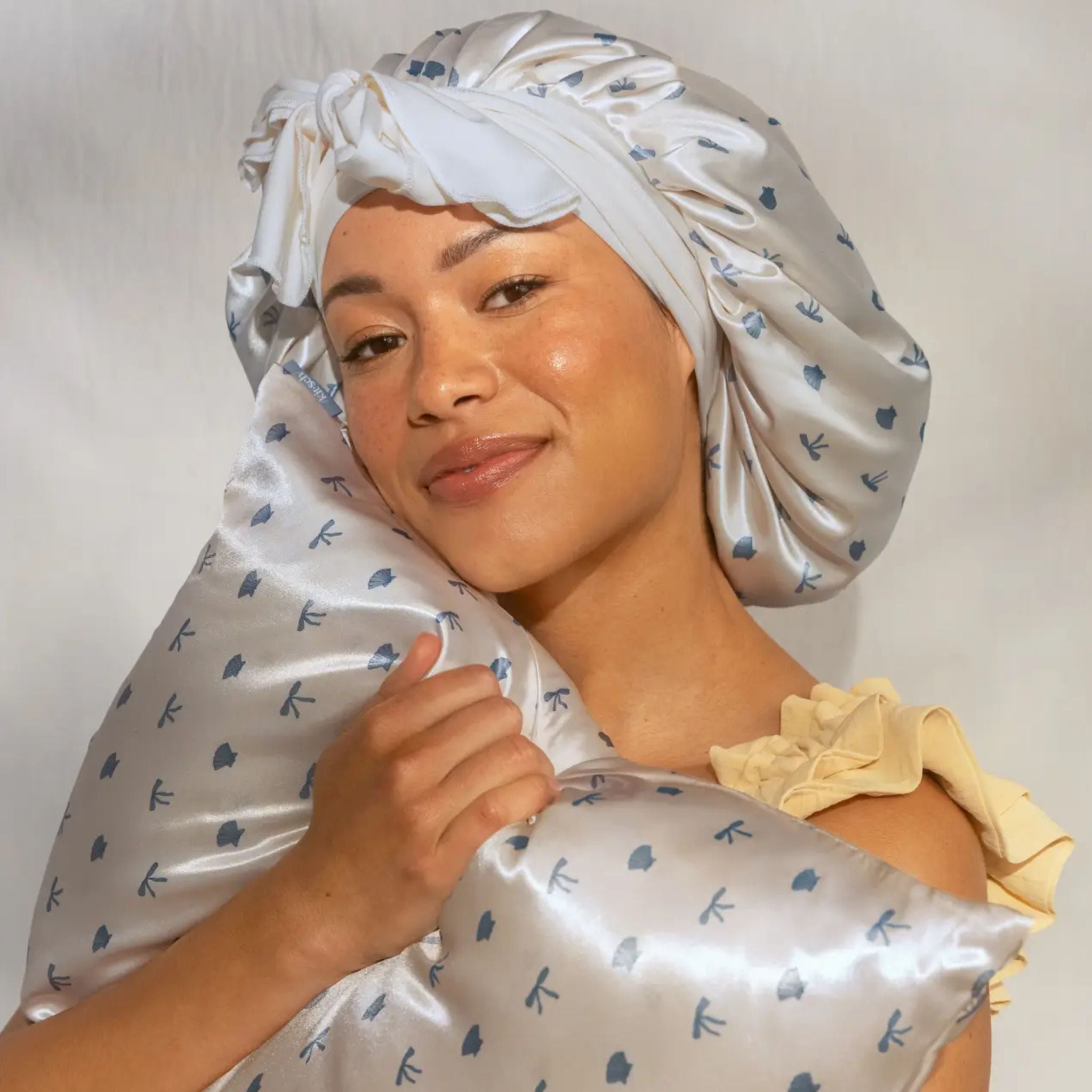 Woman wearing a satin hair cap with floral pattern against a plain background