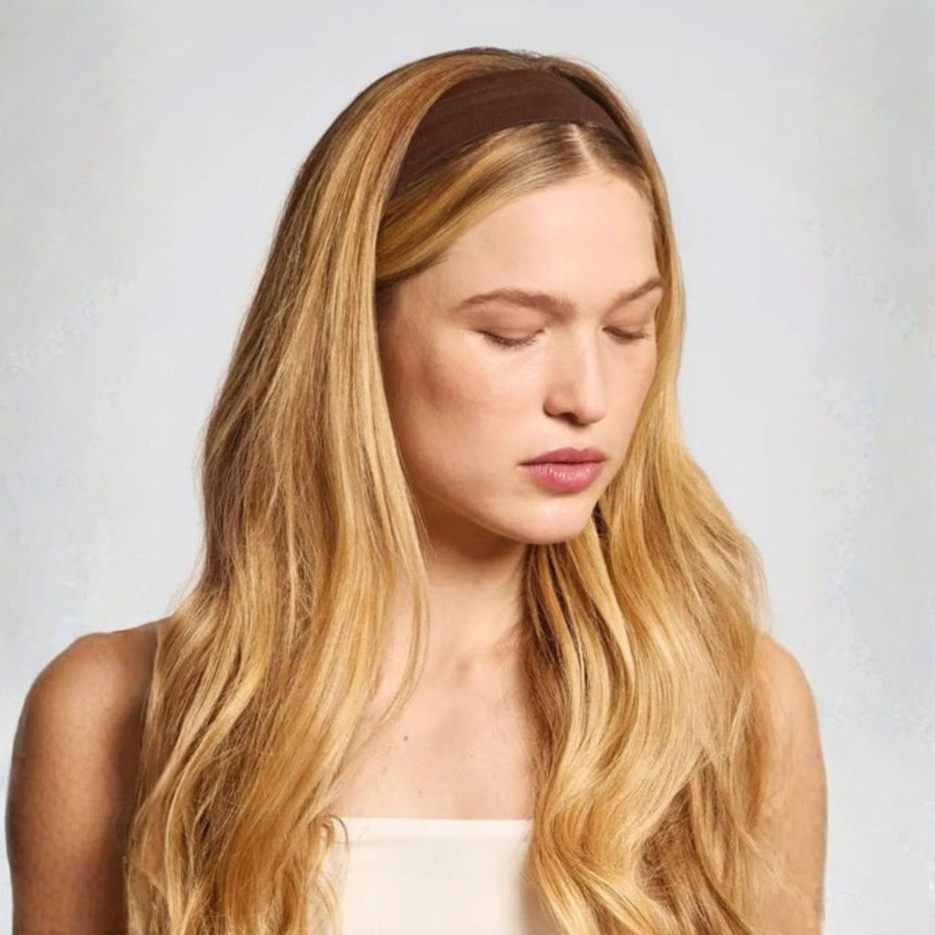 Woman with long blonde hair wearing a brown headband against a light background