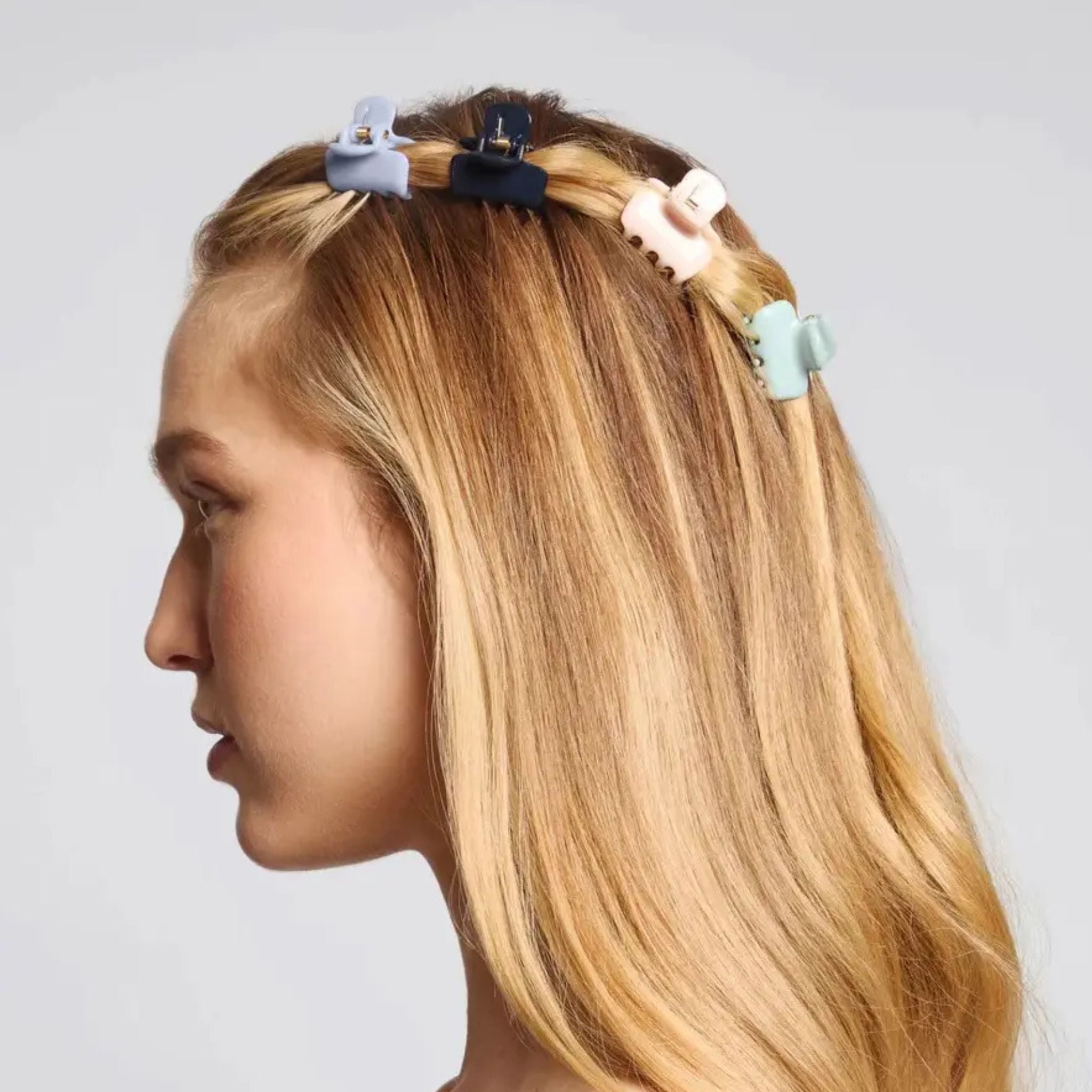 Mannequin head with blonde hair styled with colorful hair clips on a plain background