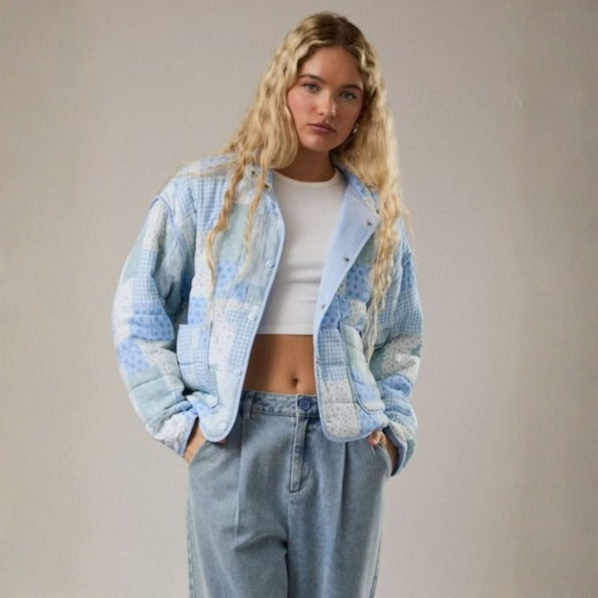 Woman wearing a light blue quilted jacket and jeans against a plain background