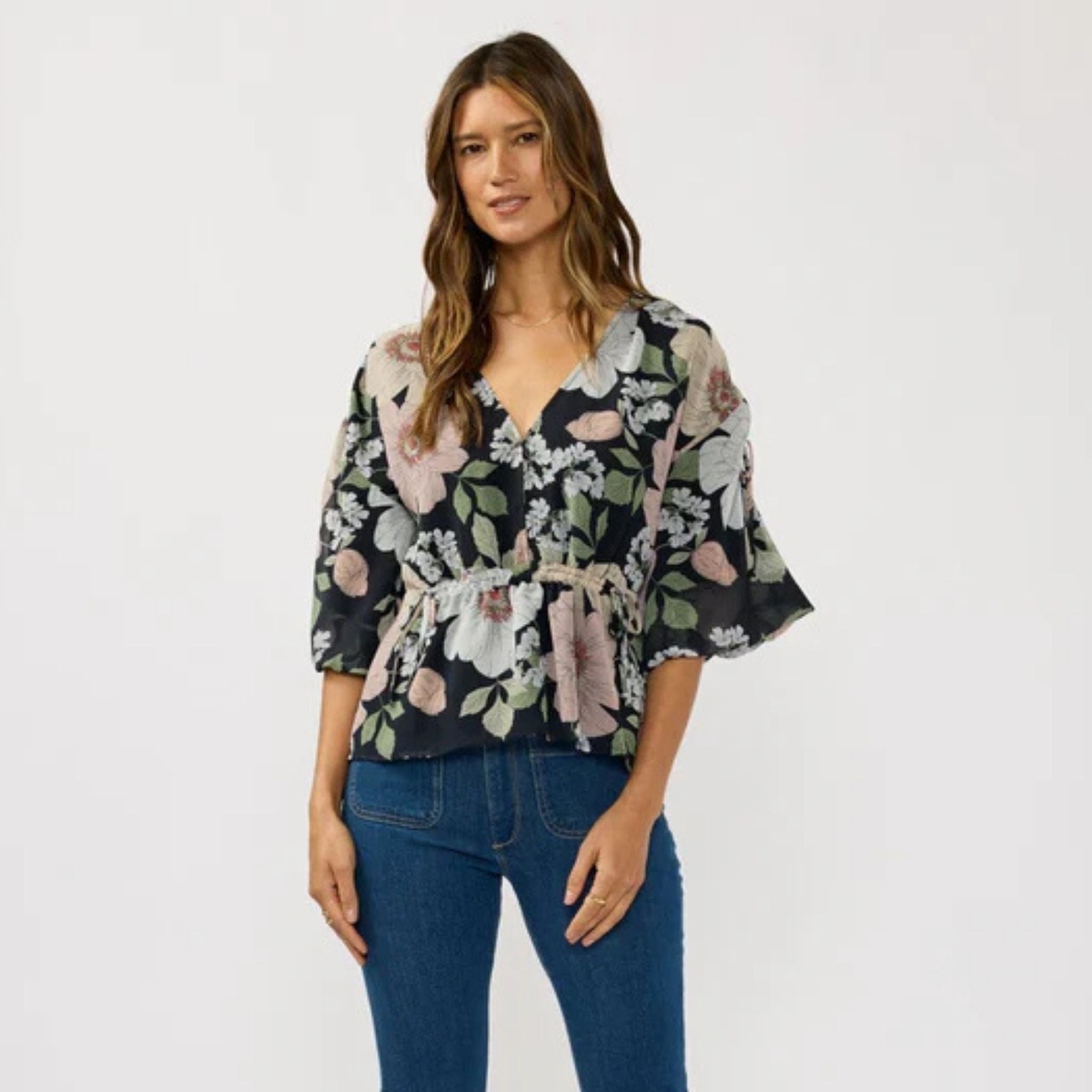 Woman wearing a floral blouse and blue jeans on a white background
